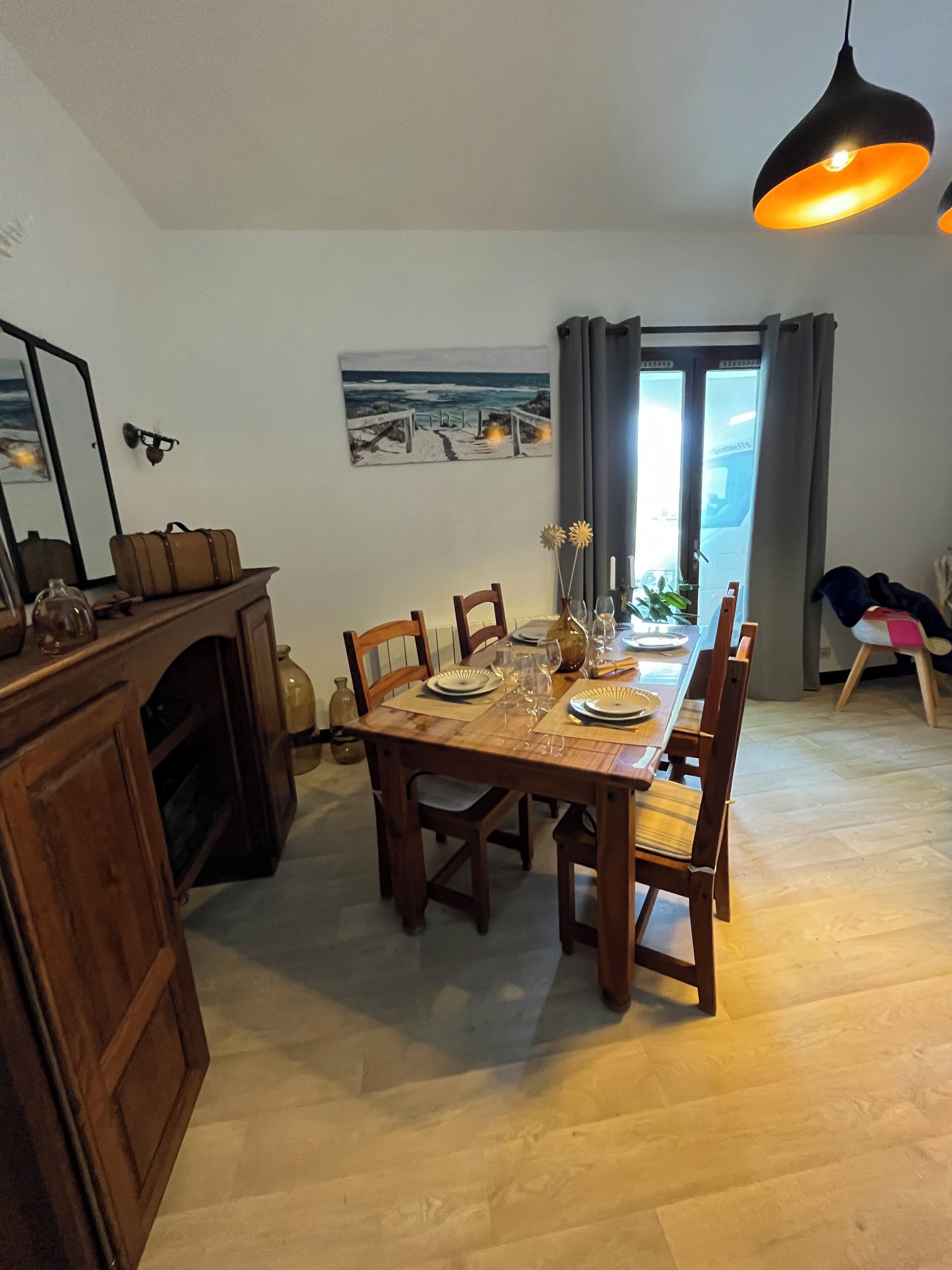 A dining area with a wooden table set for four, a mirror, and a beach-themed painting on the wall.