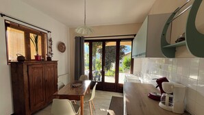 Una cuina amb taula de fusta, caires, una cafetera i vistes a través de la porta de vidre.