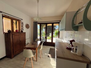 Eine Küche mit einem Holztisch, Stühlen, einer Kaffeemaschine und Blick durch die Glastür.
