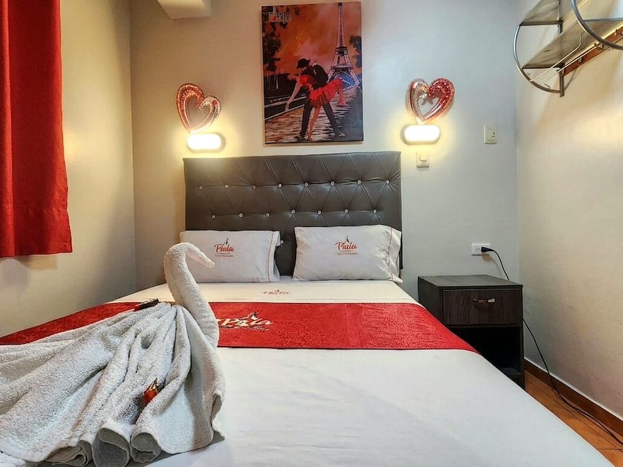 A hotel room with a bed, two heart-shaped wall sconces, a painting of the Eiffel Tower, and a red towel on the bed.