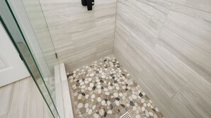 A shower with a pebble floor and a black soap dispenser.