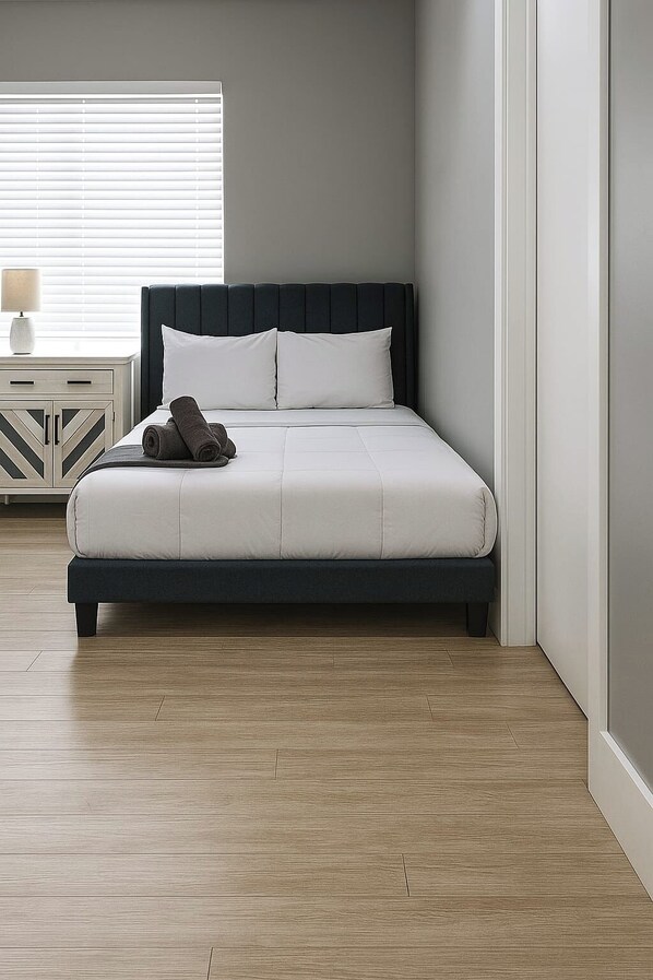 A modern bedroom with a bed, a nightstand, and a window with blinds.