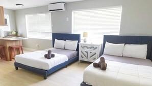 A hotel room with two beds, a desk, and a window.