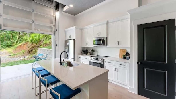 Una cocina moderna con armarios blancos, una puerta negra y una isla grande con taburetes azules.