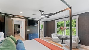 Un dormitorio moderno con una cama grande, un ventilador de techo y vistas al exterior con vegetación.