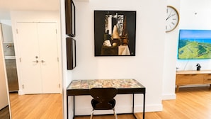 A modern room with a desk, chair, artwork, clock, and a view of the outdoors. - NYC Studio with Private Bathroom & Kitchenette (New York)