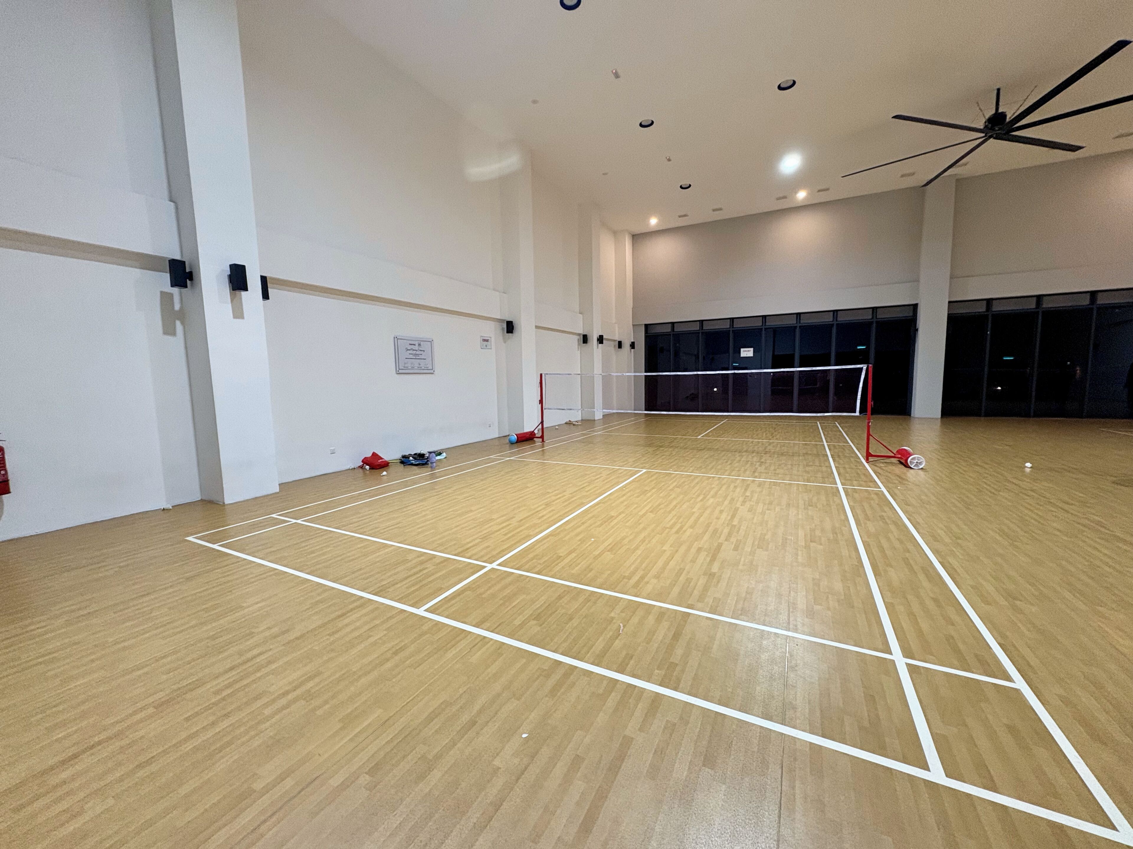 Un gimnasio interior con una red de voleibol, suelo de madera y un ventilador de techo.