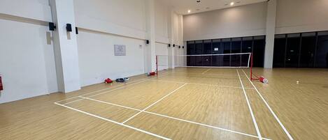 Un gimnasio interior con una red de voleibol, suelo de madera y un ventilador de techo.