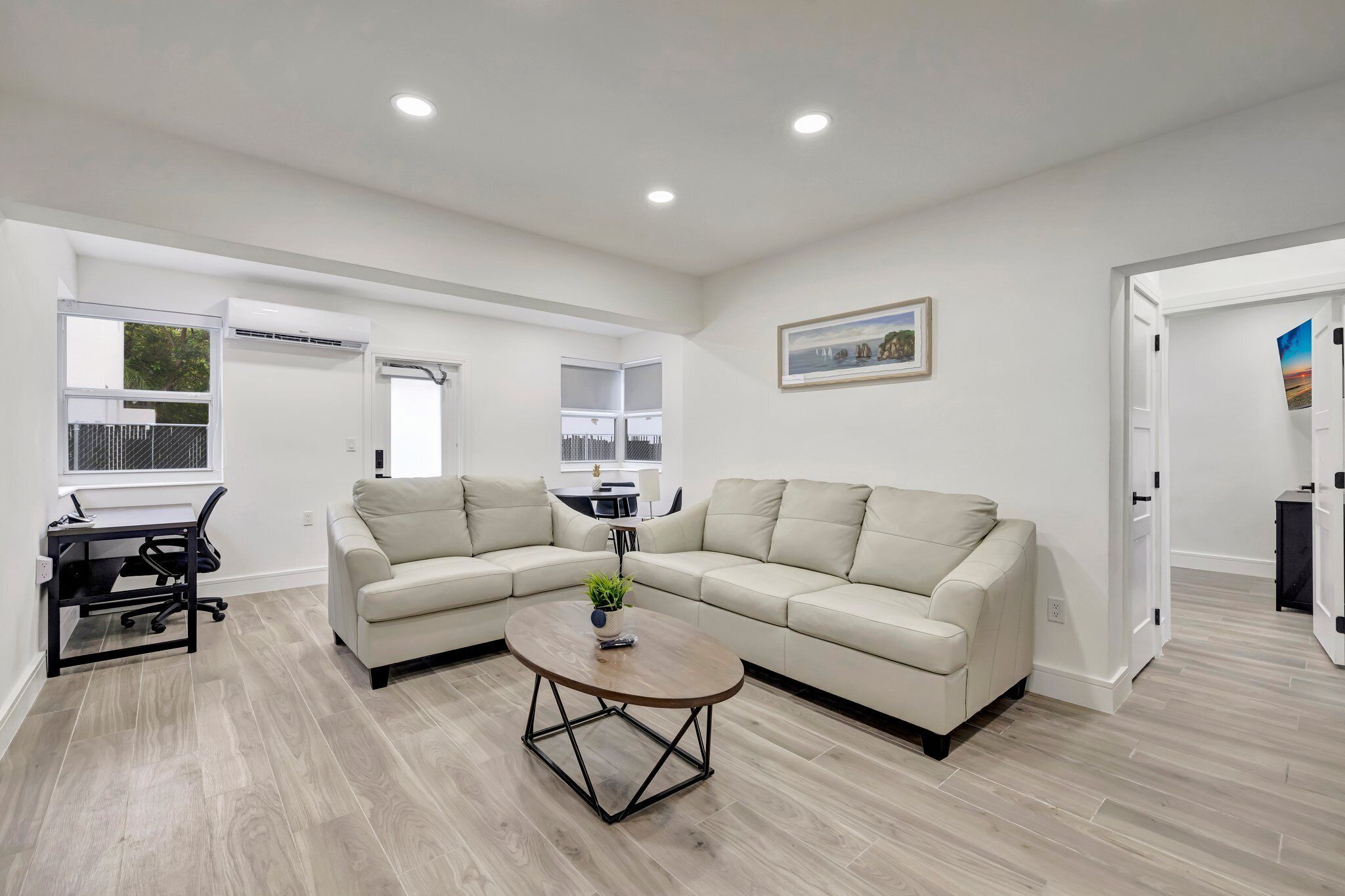 A modern living room with a beige sectional sofa, a round coffee table, and a desk with a chair.