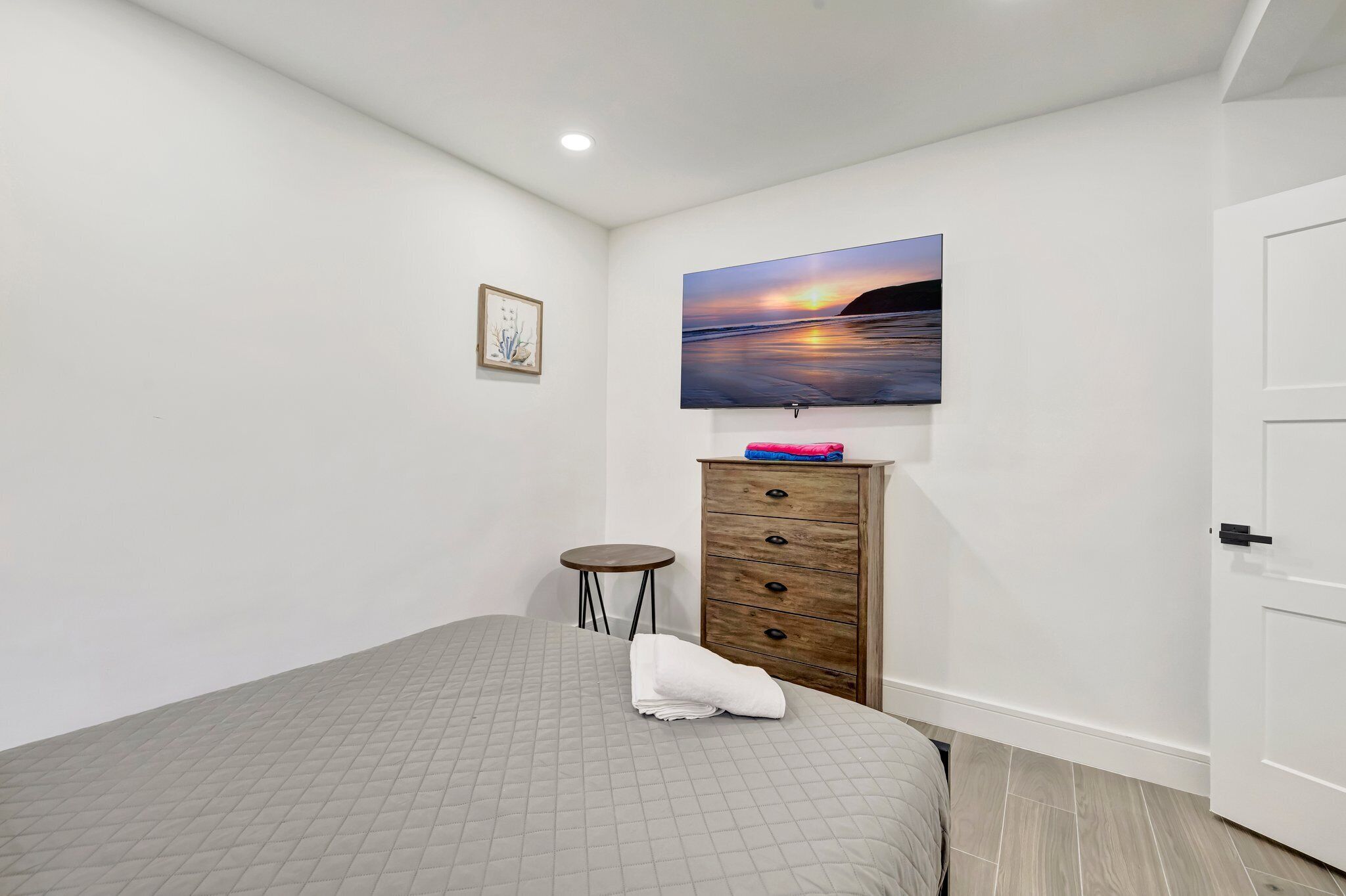 A bedroom with a bed, a dresser, a television mounted on the wall, and a door.