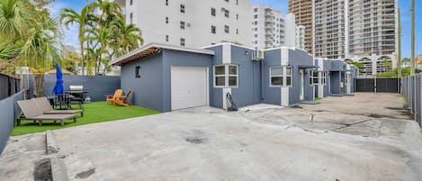 Un barrio residencial con garaje, un pequeño patio con mesa y sillas, y un césped.