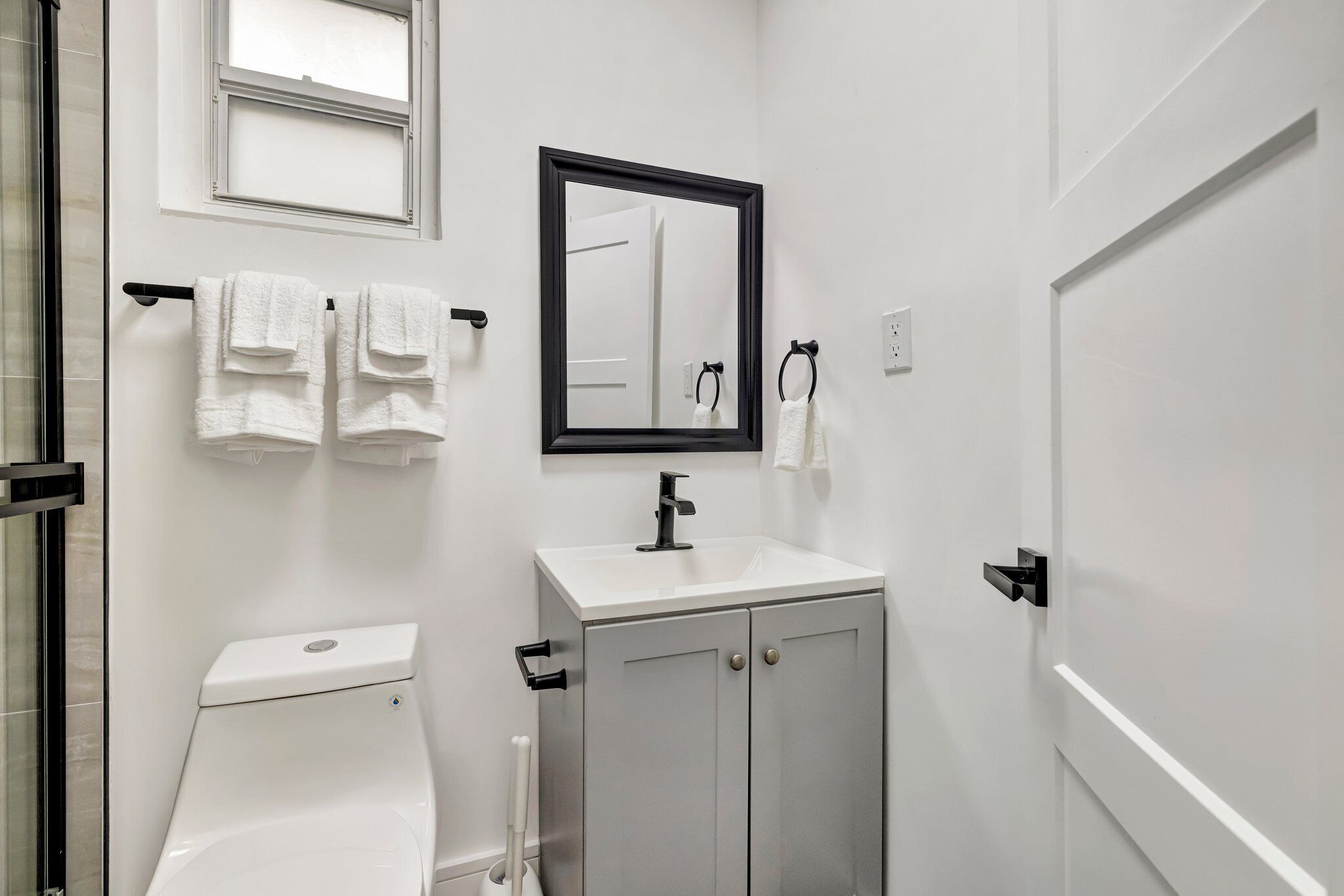 Un baño moderno con inodoro, lavamanos y mueble, que incluye un espejo y un perchero para toallas.