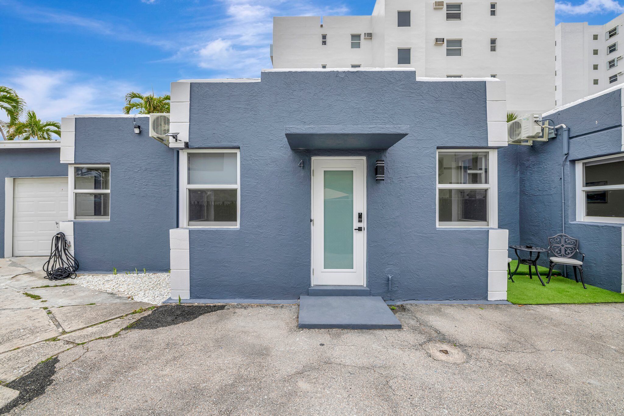 A modern building with a blue facade, a white door, and a small patio with two chairs.