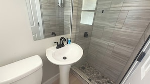 A bathroom with a pedestal sink, a toilet, and a glass shower enclosure.