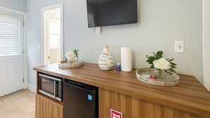 A kitchen with a microwave, refrigerator, and a flat-screen TV mounted on the wall.