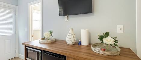 A kitchen with a microwave, refrigerator, and a flat-screen TV mounted on the wall.