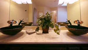 Een badkamer met een grote spiegel, twee wasbakken, een plant in pot en een handdoek op het aanrecht.