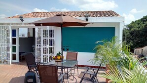 Un patio al aire libre con una mesa y sillas, un paraguas grande y vistas a un edificio con techo de tejas.