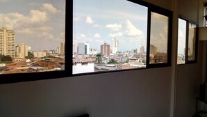 Vista desde el interior de un edificio, a través de una ventana, mostrando un paisaje urbano con diversos edificios, incluyendo estructuras de gran altura y viviendas más pequeñas.