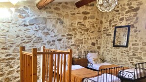 A rustic bedroom with a stone wall, a wooden gate, two metal beds, and a hanging light fixture. - Typical house in the historic center of the Arles bullring (Arles)
