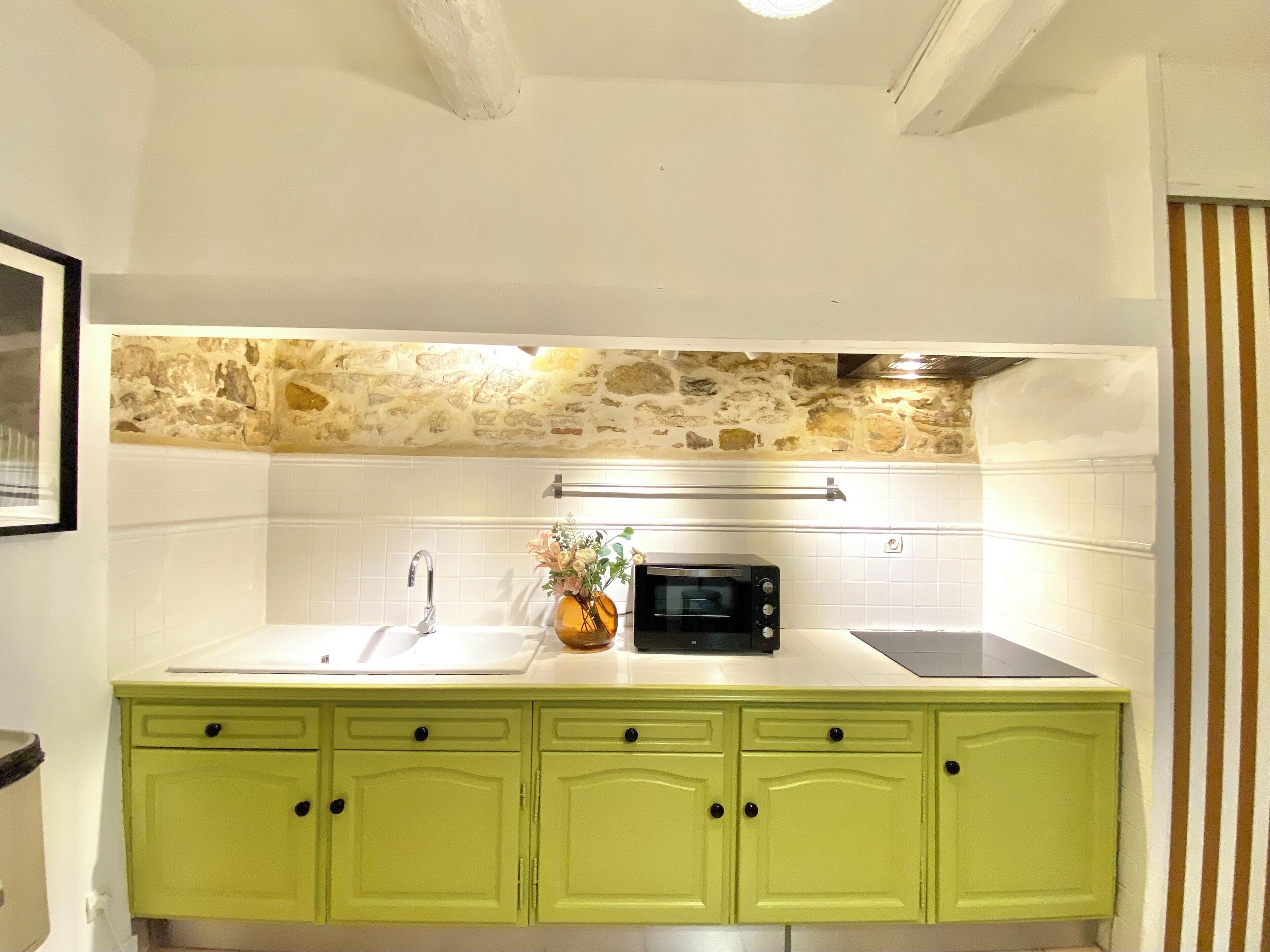 A kitchen with a stone backsplash, a microwave, a sink, and green cabinets.