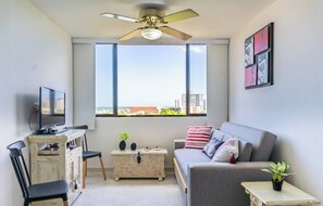 A modern living room with a grey sofa, a small table, a TV, and a ceiling fan.