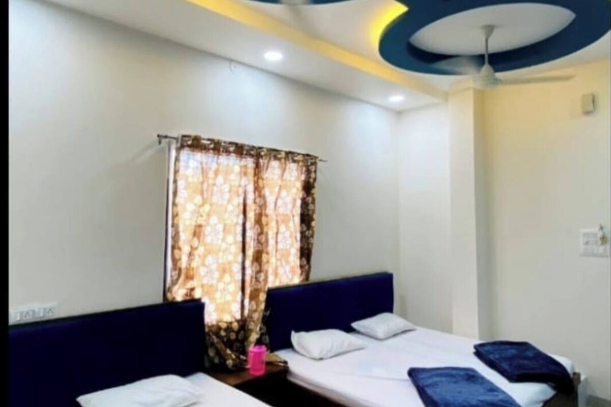 A hotel room with two beds, each with a headboard and pillows. The room has a modern ceiling design with circular patterns and recessed lighting.