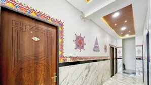 A hallway with a marble floor, a wooden door with a number plate, and decorative wall art. - Hotel Tirupati Ujjain  (Ujjain)