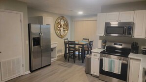 Cozinha compacta com geladeira, micro-ondas, fogão e área de refeições com cadeiras e mesa.