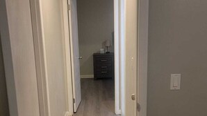 Um corredor com piso de madeira, paredes brancas e um aparador escuro ao fundo.