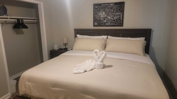 Cama bem arrumada com um par de toalhas brancas dobradas no centro, uma cabeceira de madeira escura e um mapa de Paris na parede acima.