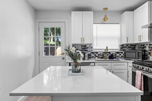 A modern kitchen with white cabinetry, a central island, and a view of the outdoors through a window. - Cozy Home near NRG, Medical Centre, Toyota Centre with Hot Tub Spa, Arcade, BBQ (Houston)