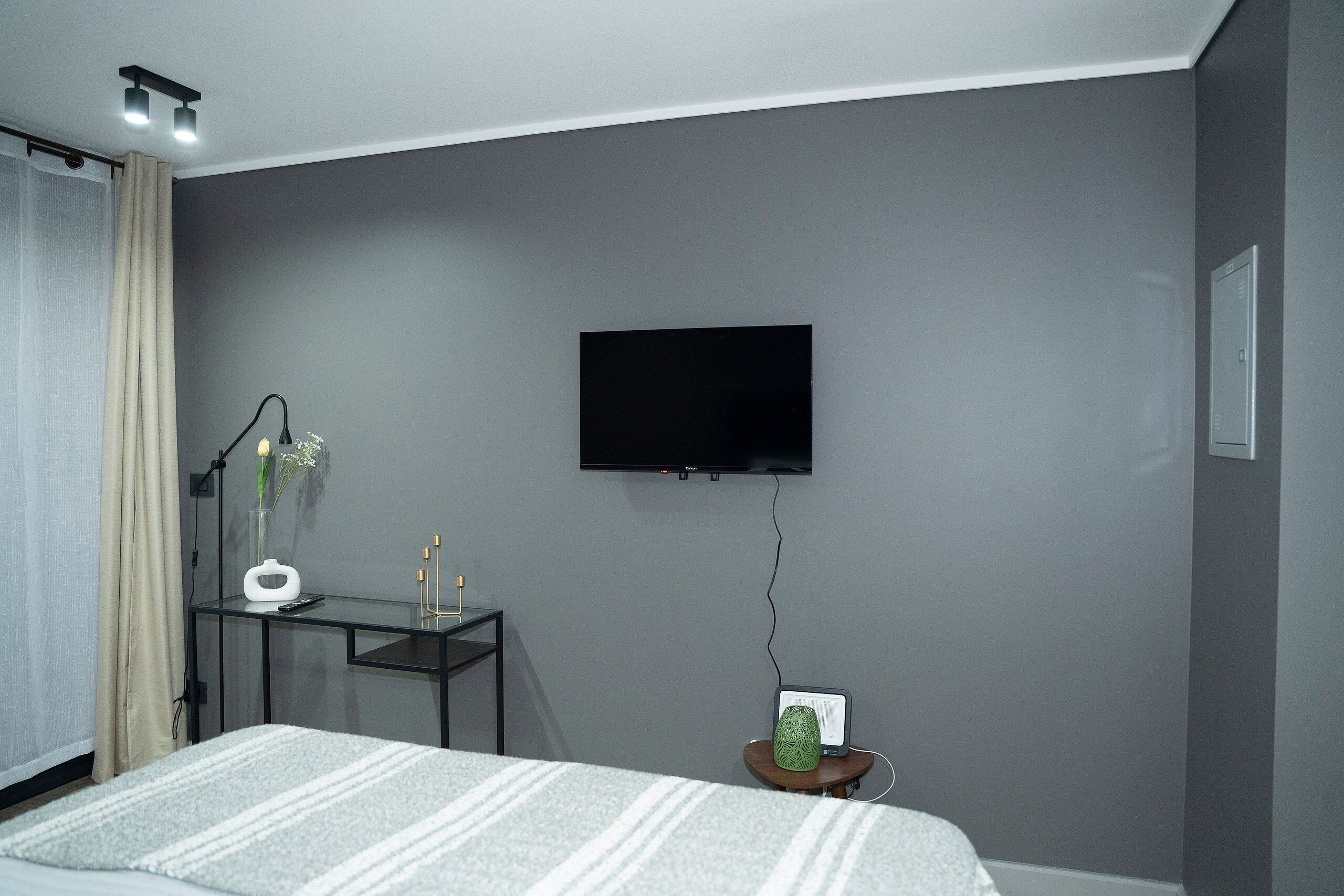 Una camera da letto moderna con un letto, una scrivania, una televisione e un tavolino con una pianta.