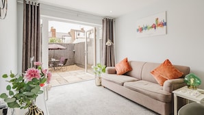 A living room with a sofa, cushions, a small table, and a vase with flowers. - The Nook, Fairview, Cheltenham Town Centre - Parking & Garden (Cheltenham)