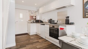 A modern kitchen with white cabinetry, a built-in oven, and a dining area with a table set for two. - The Nook, Fairview, Cheltenham Town Centre - Parking & Garden (Cheltenham)