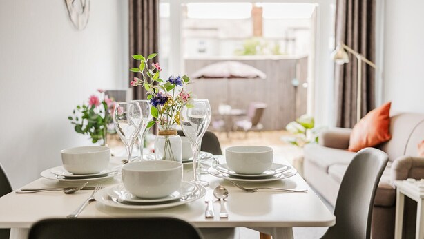 A dining table set with white plates, bowls, and clear wine glasses, accompanied by a vase of flowers. - The Nook, Fairview, Cheltenham Town Centre - Parking & Garden (Cheltenham)