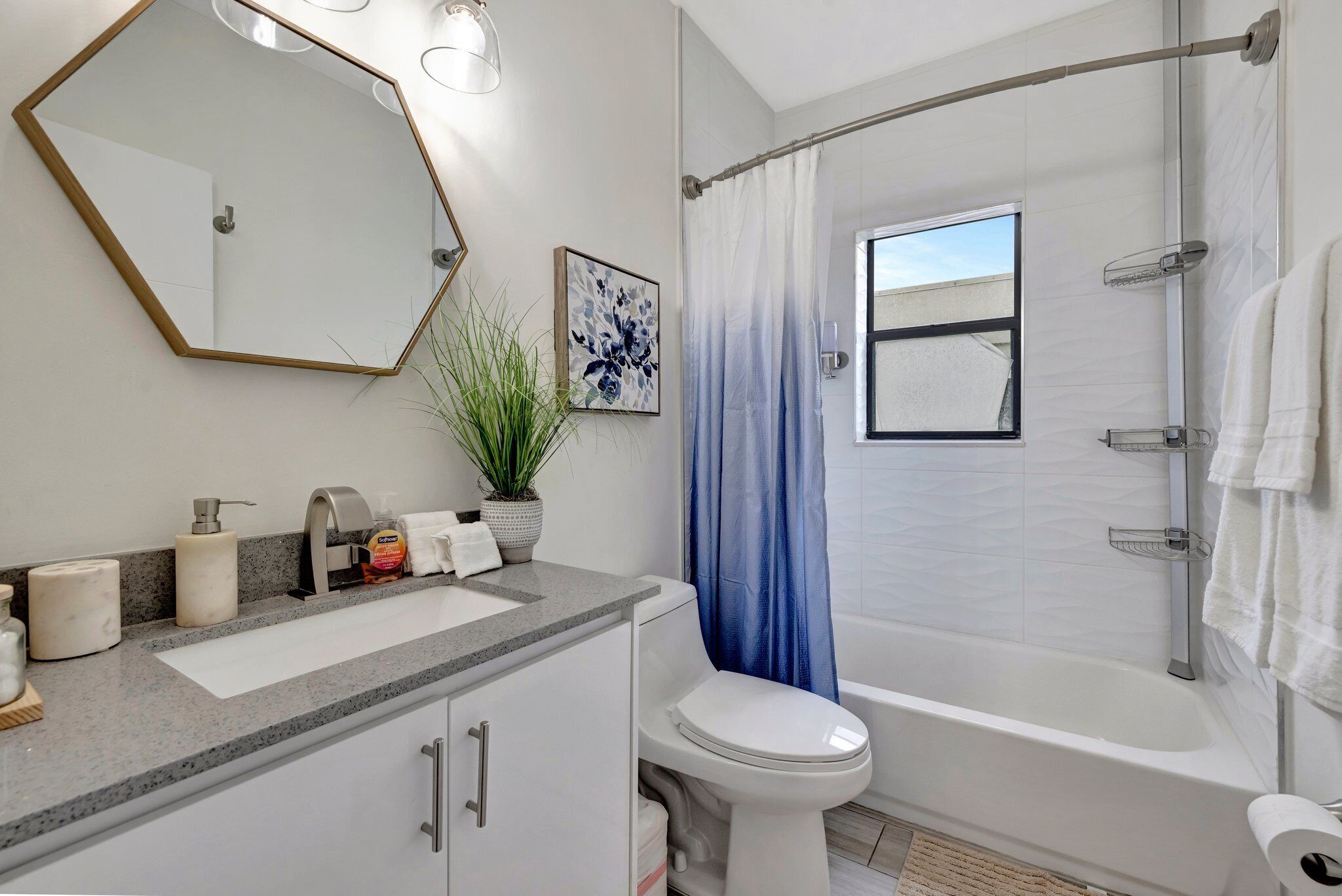 Un baño moderno con un espejo grande, un lavamanos, un inodoro y una bañera.