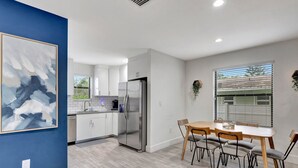 Eine moderne Küche mit weißen Schränken, einem Edelstahl-Kühlschrank und einem Essbereich mit Holztisch und -stühlen.