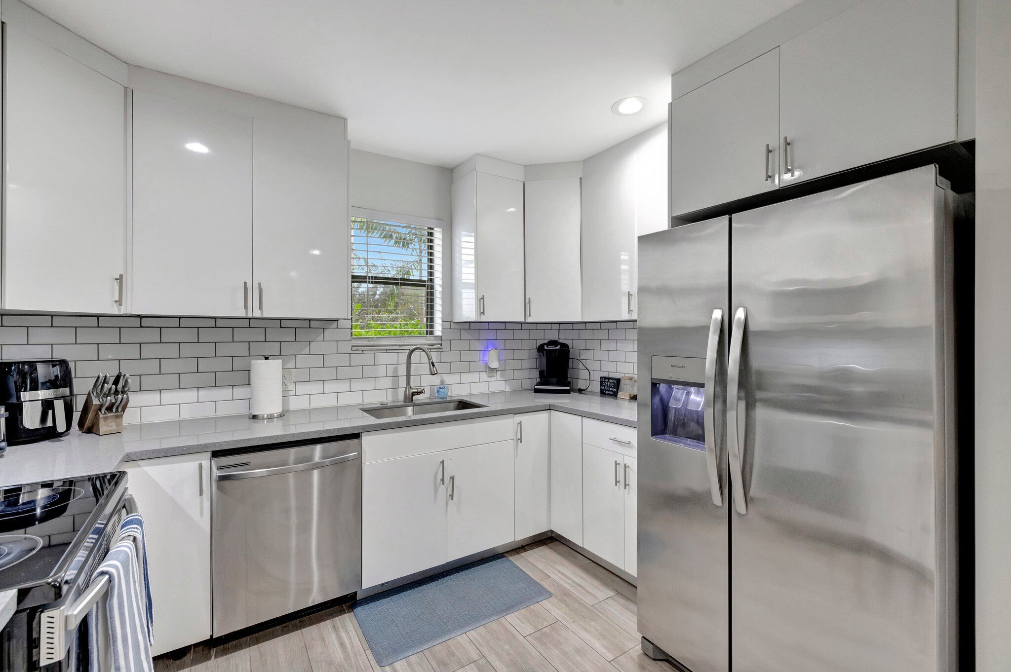 A modern kitchen with white cabinets, stainless steel appliances, and a window with blinds.