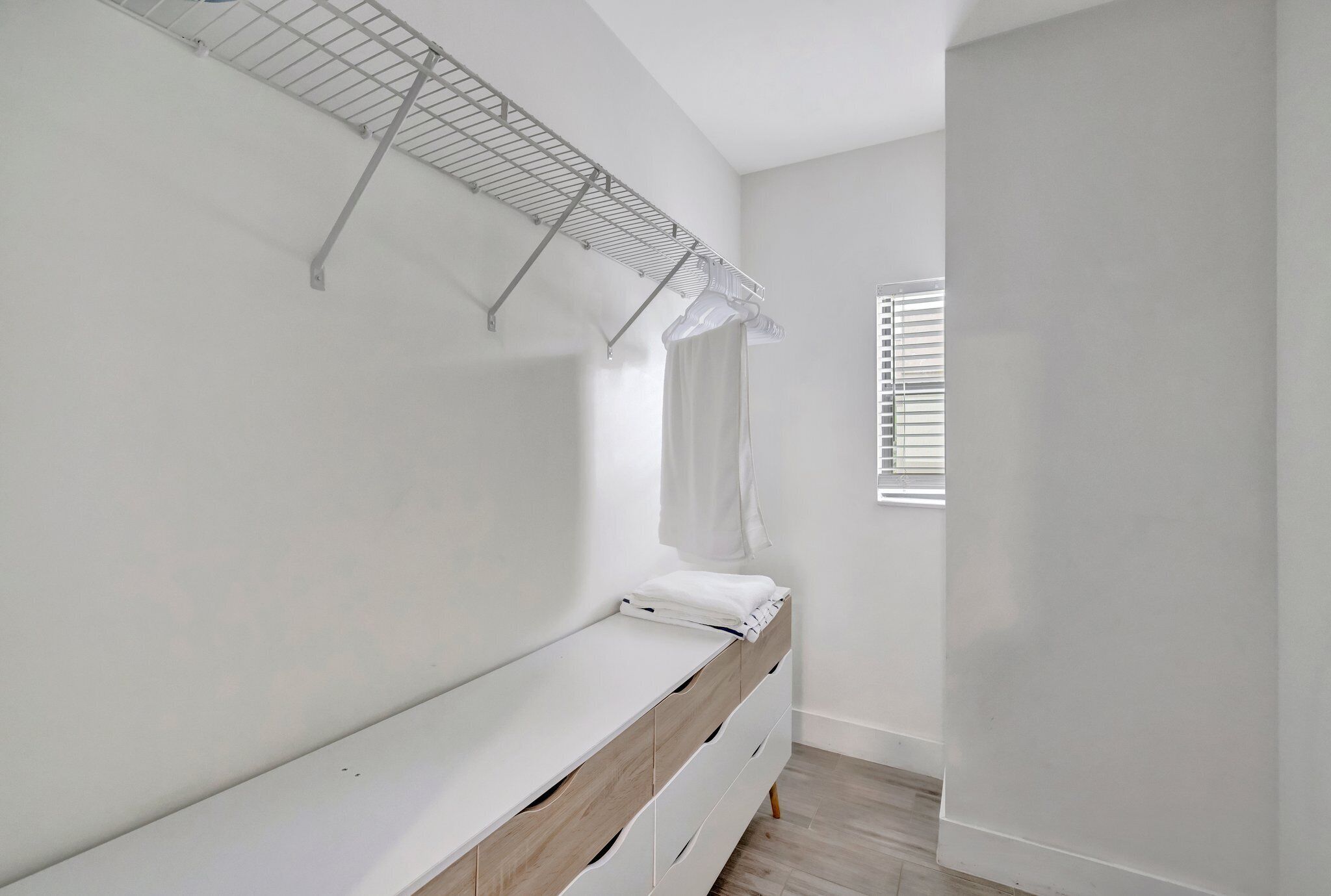 Ein Zimmer mit einem weißen Babybett, einem Metallregal und einem Fenster mit Jalousien.