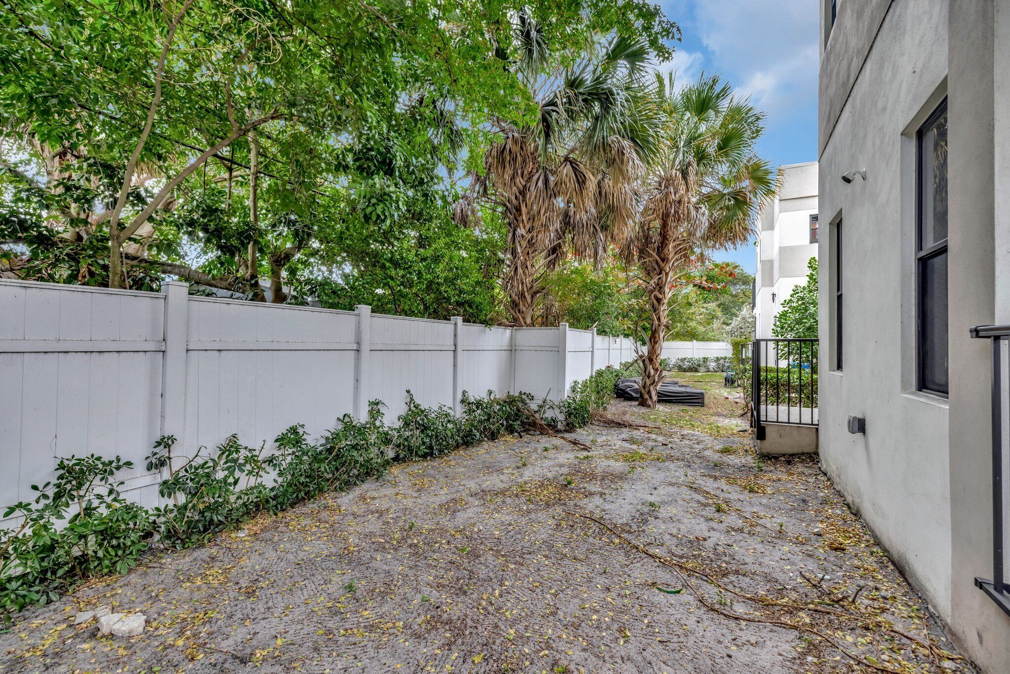 Un patio empedrado con cerca blanca, árboles y un edificio con ventanas.