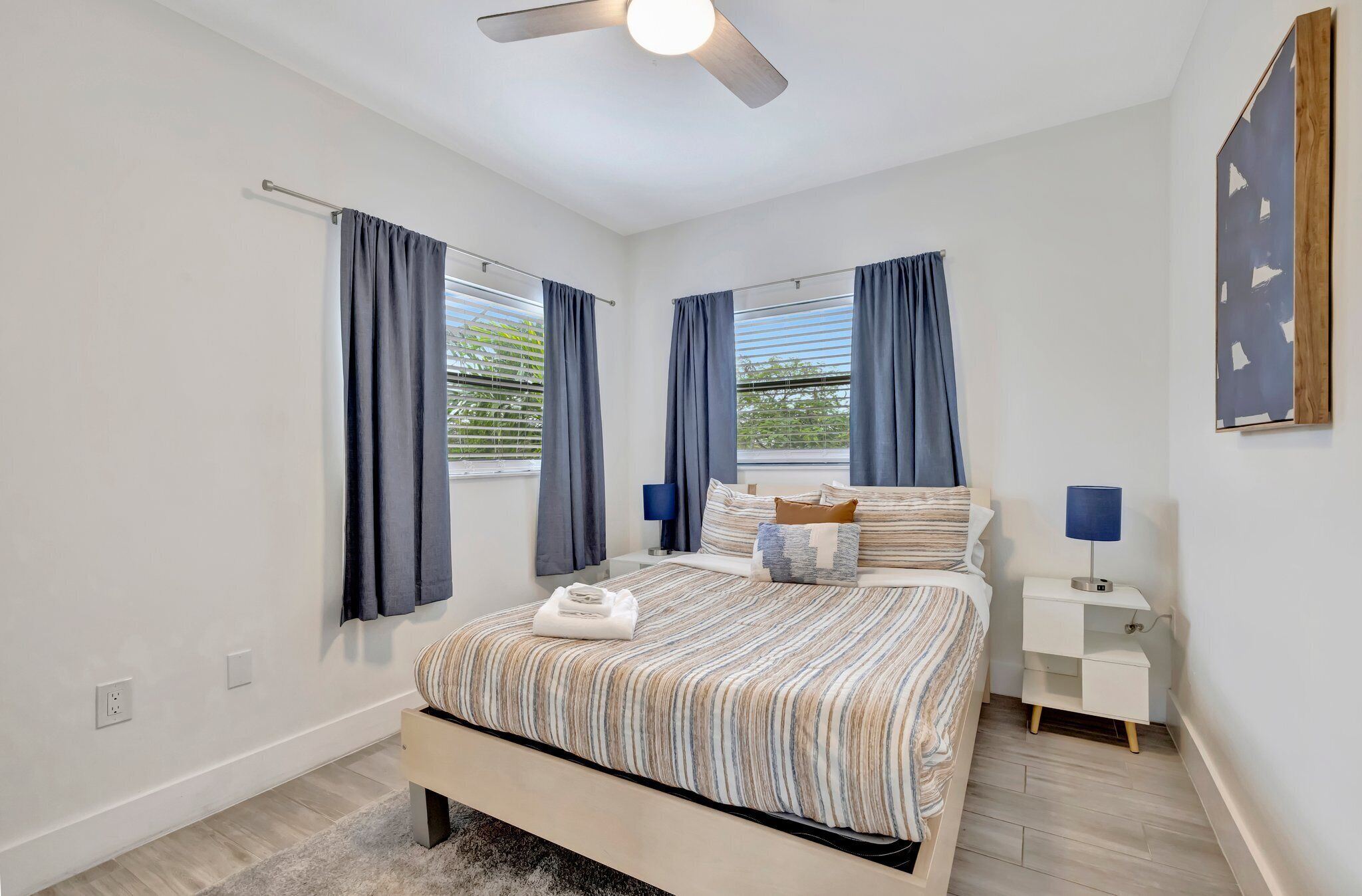 A modern bedroom with a bed, a nightstand, a ceiling fan, and a window with curtains.