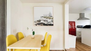 Ein Essbereich mit Holztisch und gelben Stühlen, ein roter Kühlschrank und eine Küche im Hintergrund.