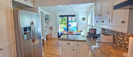A modern kitchen with white cabinetry, a stainless steel refrigerator, a granite countertop, and a view of a patio with outdoor seating.