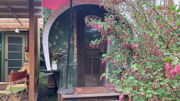 A wooden deck with a red umbrella, a door with floral wallpaper, and a bench.