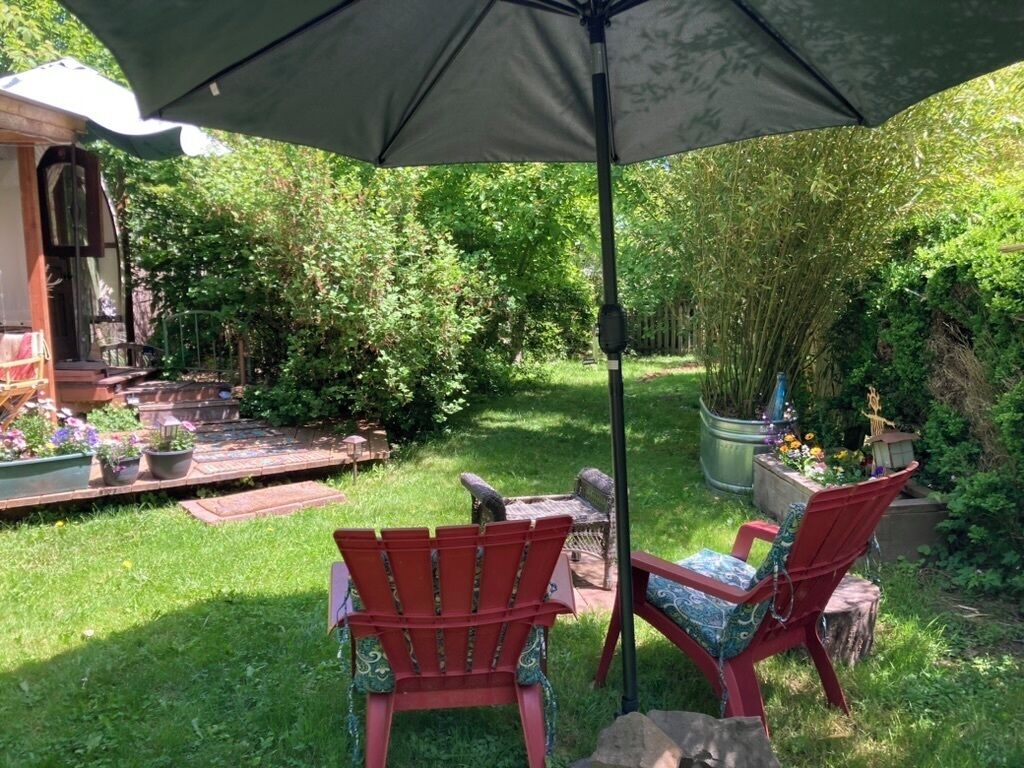 A patio area with two red Adirondack chairs, a table, and a large umbrella.