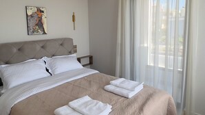 Una habitación de hotel moderna con una cama grande, cabecera, mesita de noche, un cuadro en la pared y cortinas translúcidas en la ventana.