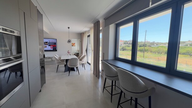 Una cocina moderna con zona de comedor, ventanas amplias y vistas a zonas verdes.