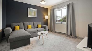 Ein modernes Wohnzimmer mit einem grauen Sofa, einem kleinen weißen Couchtisch und einem Fernseher auf einem Schrank.