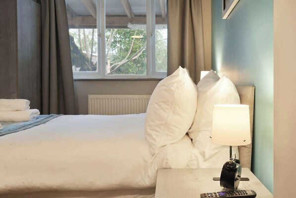 A hotel room with a bed, pillows, a lamp, and a remote control on a nightstand.